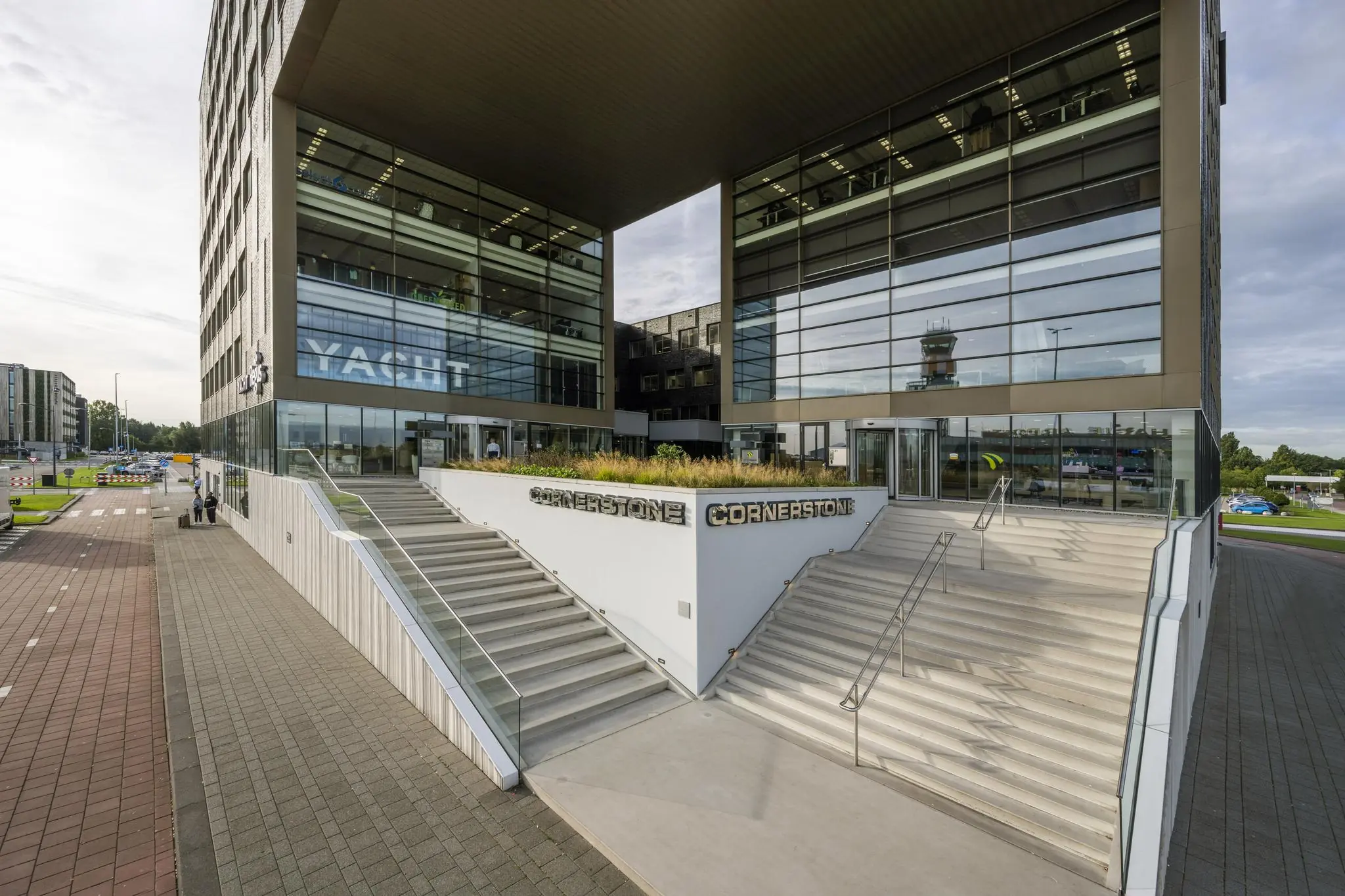 Hoofdentree van het moderne Cornerstone kantoorgebouw aan het Airportplein in Rotterdam, met brede trappen en glazen gevels.